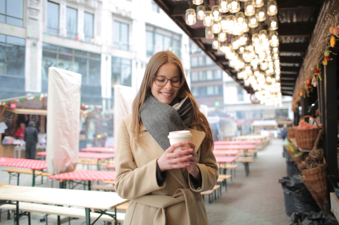 services-01 Smiling woman holding a coffee outdoors at a market with warm lighting.